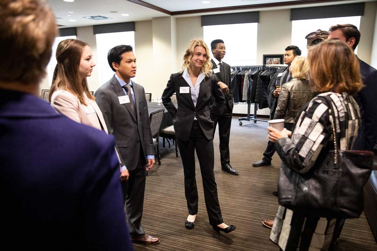 A small group of people including men and women dressed in business attire stand and talk to each other