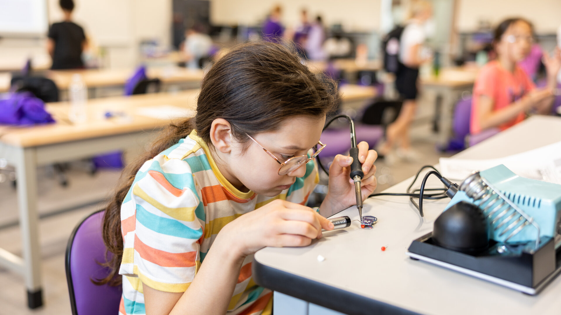 young girl solders parts on a robot