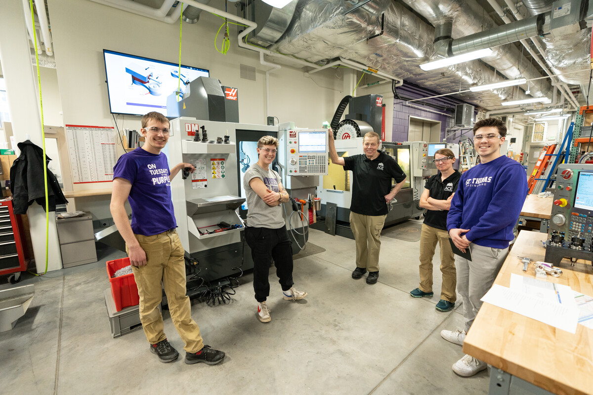 Engineering faculty and students stand beside CNC machinery
