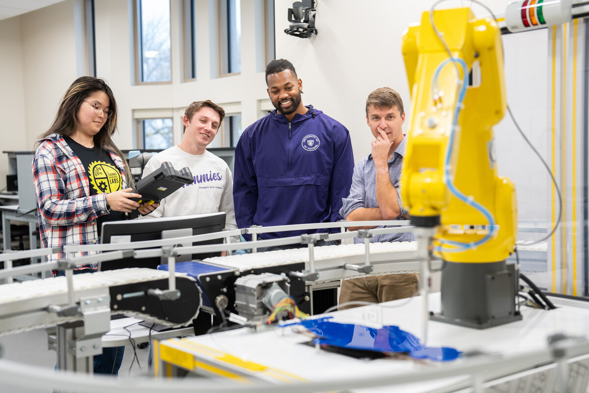 Engineering students stand holding a controller of a robotic arm.