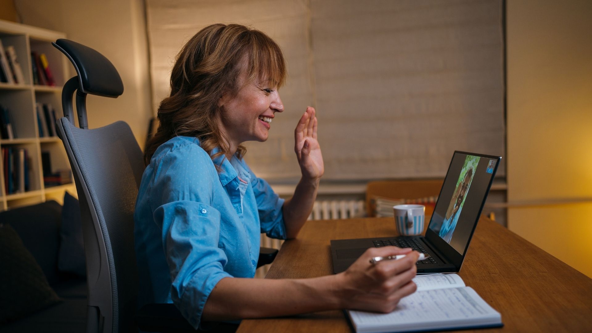 smiling woman waves during an online meeting