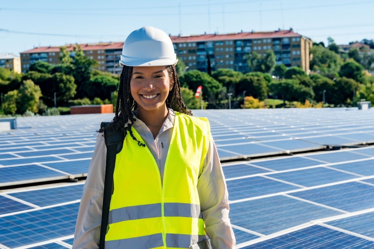 renewable energy technician stands in front of an array of rooftop solar panels
