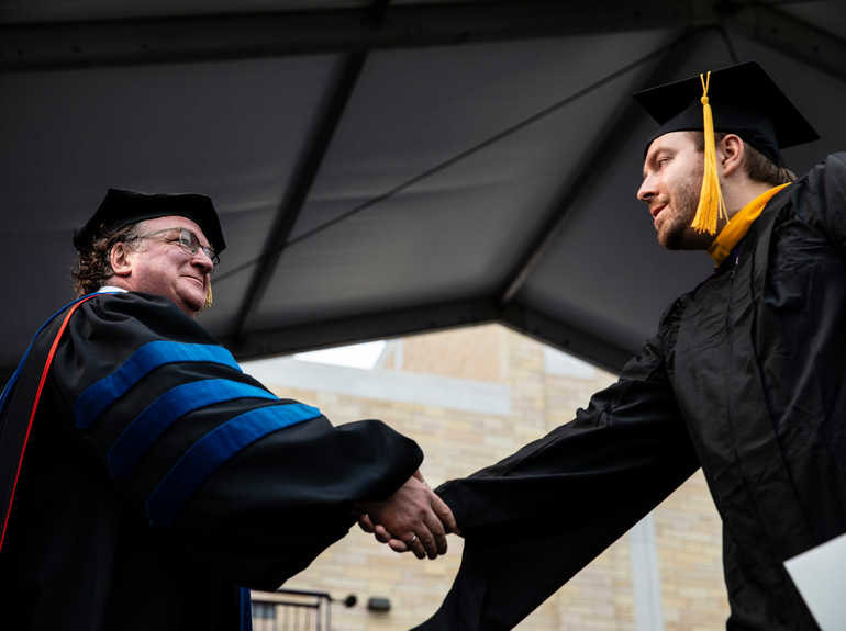Dean shakes students hand during graduation ceremony.