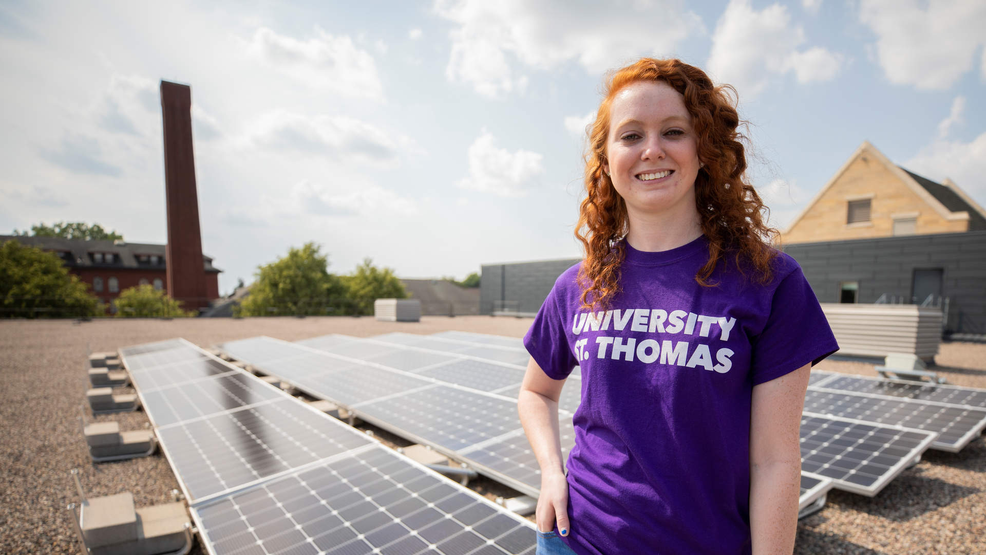 St. Thomas Electrical Engineering student stands on the roof next to the microgrid's solar array.