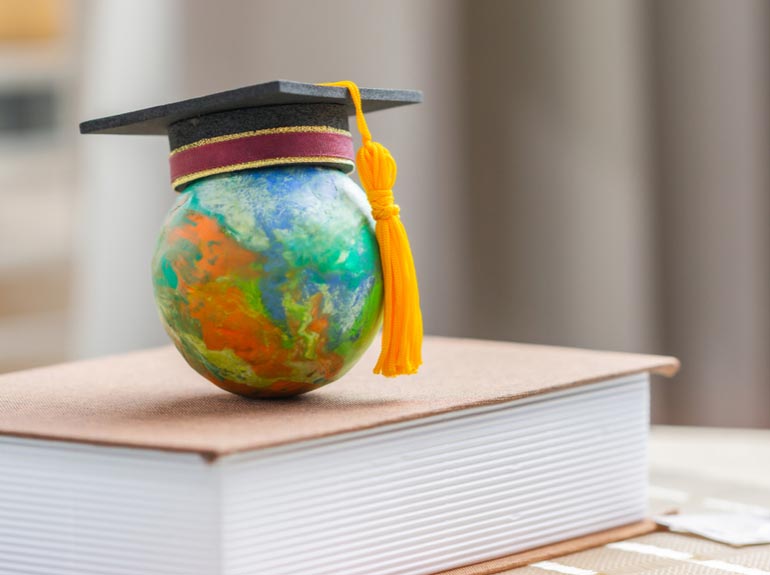 Globe with a graduation cap sits onto of a book