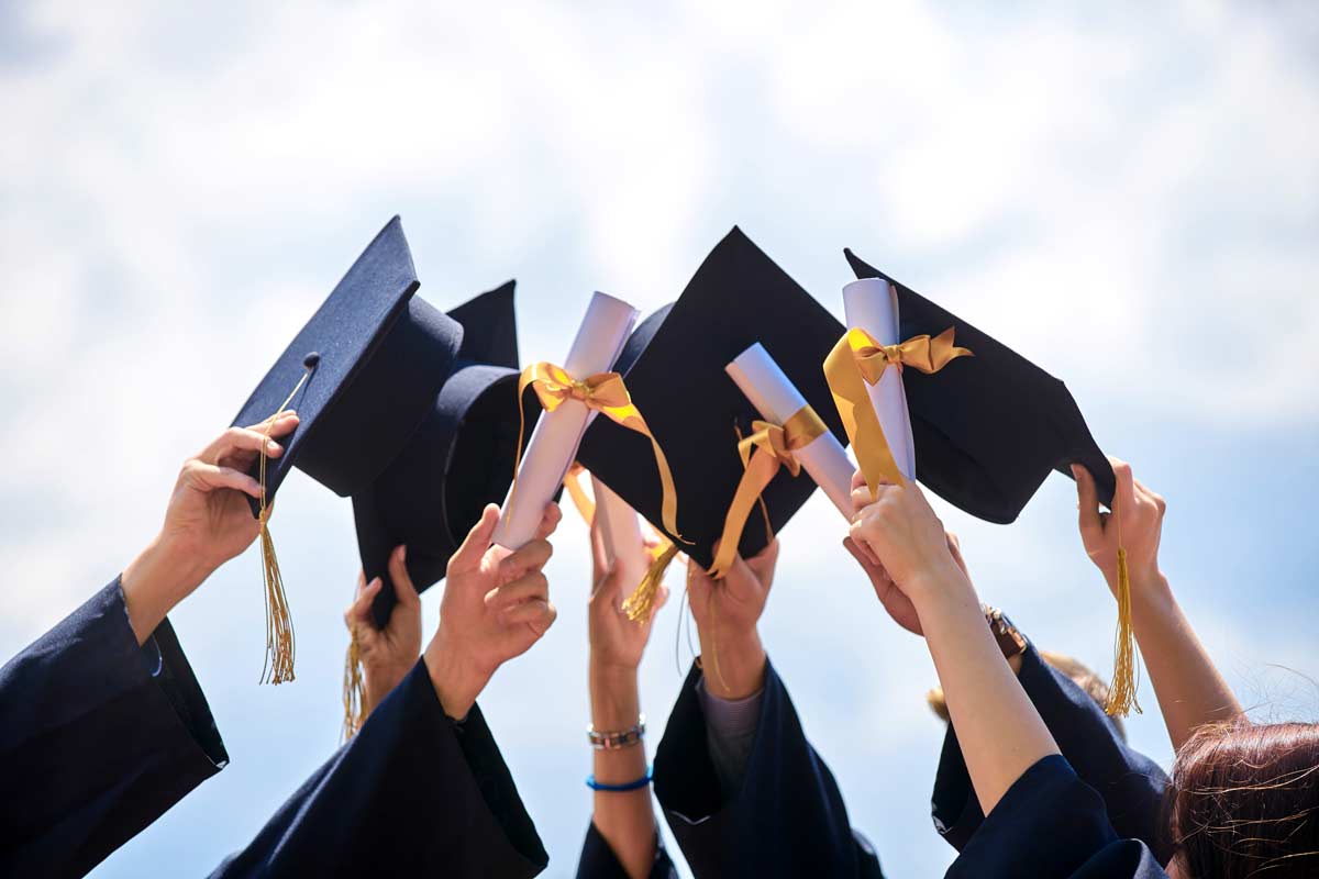 Individuals holding graduation caps in the air.