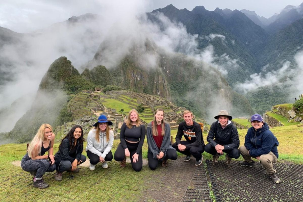 A group of students sit at the base of mountains in Peru.